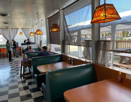 Interior of a diner with checkered floors, booths, and pendant lamps, featuring customers and a bright, airy atmosphere.