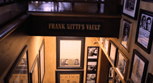 A staircase leading to "Frank Nitti's Vault," surrounded by historical photos and documents on the walls.