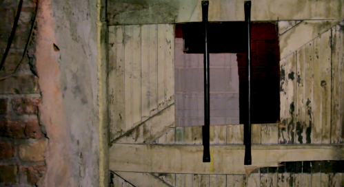 A weathered wooden door with a barred window, set against a rough stone wall.
