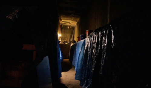 Dimly lit hallway with blue tarps lining the walls, creating a mysterious and shadowy atmosphere.