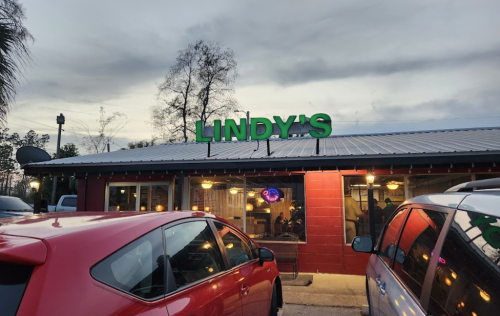 Exterior of Lindy's restaurant at dusk, featuring a red building, green sign, and parked cars in front.