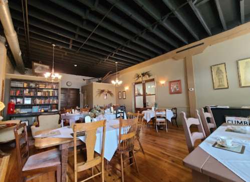 Cozy restaurant interior with wooden tables, chairs, and bookshelves, featuring warm lighting and a welcoming atmosphere.