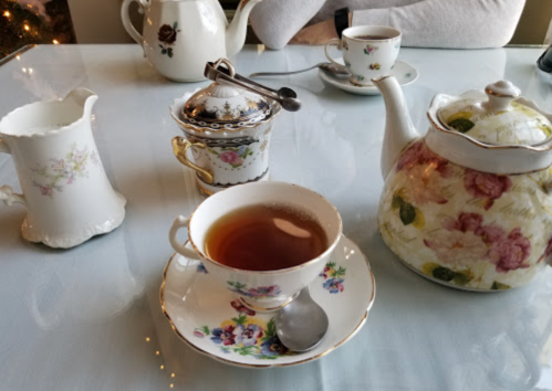 A delicate tea set with a floral teapot, cup, and saucer, accompanied by a sugar bowl and cream pitcher on a table.