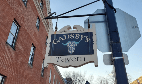 Sign for Gadsby's Tavern, established in 1785, featuring a grapevine design, hanging from a post.