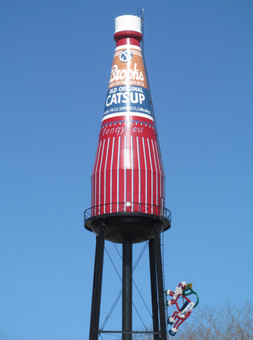 A large water tower shaped like a ketchup bottle, painted red with white stripes and the brand name "Brooks."
