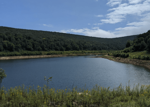 A serene lake surrounded by lush green hills under a partly cloudy sky.