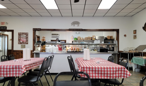 Interior of a casual restaurant with checkered tablecloths, a counter displaying food, and a cozy, welcoming atmosphere.