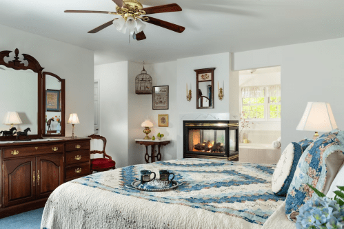 Cozy bedroom with a quilted bed, fireplace, vintage furniture, and soft lighting, creating a warm atmosphere.