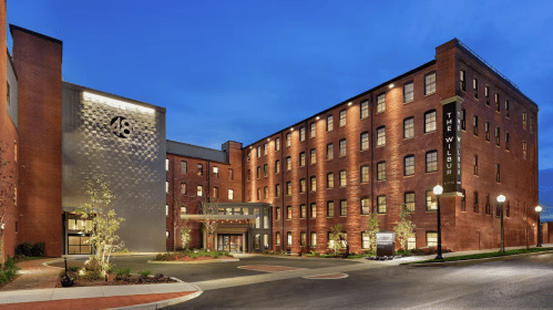 A modern brick hotel building at dusk, featuring a stylish entrance and illuminated signage.