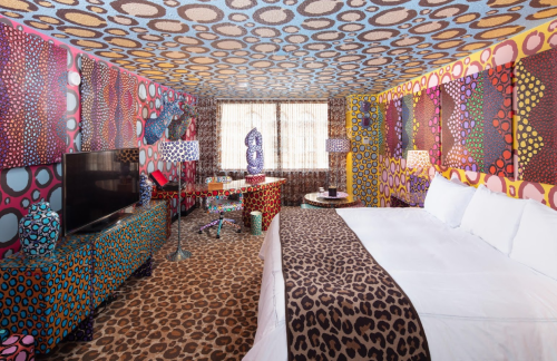 A vibrant hotel room with colorful patterned walls, a leopard print bedspread, and unique decorative lamps.