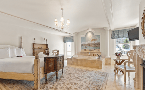 Spacious hotel room with a king bed, vintage furniture, a large bathtub, and elegant decor.