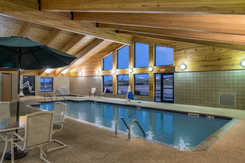 Indoor swimming pool with wooden beams, lounge chairs, and large windows overlooking a scenic view.