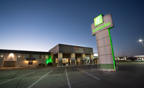 Holiday Inn exterior at dusk, featuring a lit sign and empty parking lot.