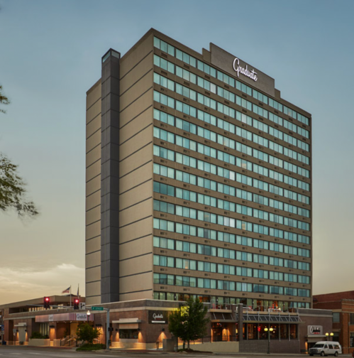 A tall hotel building with large windows, featuring the name "Graduate" on the top, set against a clear sky.