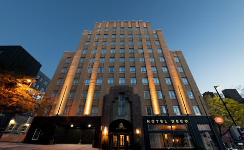 Art Deco hotel exterior at dusk, featuring illuminated architectural details and a welcoming entrance.