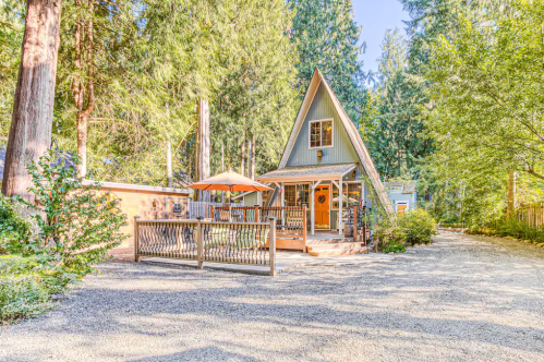 A charming A-frame cabin surrounded by tall trees, featuring a deck and outdoor seating area.