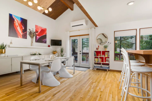 Bright dining area with modern furniture, large windows, and wooden beams, featuring a table set for a meal.