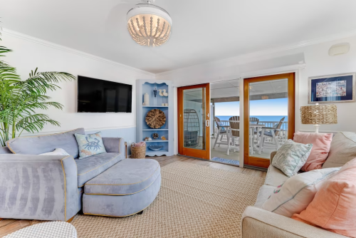 Cozy living room with blue furniture, a TV, and sliding doors leading to a patio with ocean views.