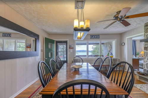 A cozy dining area with a wooden table, black chairs, and a view of the lake through large windows.