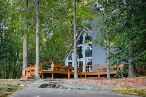 A modern A-frame cabin surrounded by trees, featuring large windows and a wooden deck.
