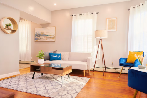 Bright living room with a gray sofa, blue accent chair, wooden coffee table, and large windows letting in natural light.