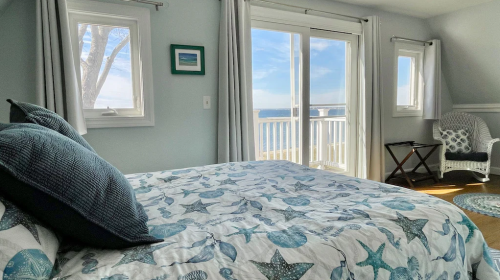 Cozy bedroom with a starfish-patterned bedspread, large windows, and a view of the water.
