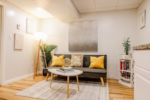 Cozy living room with a gray sofa, yellow pillows, a round coffee table, and a lamp, featuring light wood flooring.