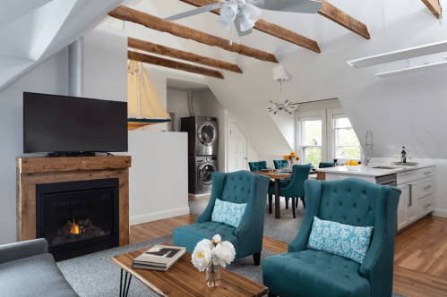Cozy living space with teal chairs, a fireplace, and a dining area, featuring wooden beams and modern appliances.