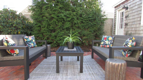 Cozy outdoor seating area with two chairs, a table, and a potted plant, surrounded by greenery.