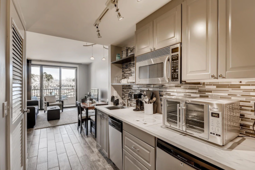 Modern kitchen with stainless steel appliances, sleek cabinets, and a view of a balcony through large windows.