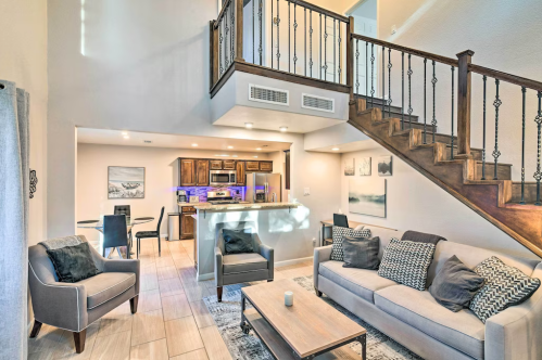 Modern living room with a staircase, featuring a cozy sofa, armchairs, and a kitchen area with stylish decor.