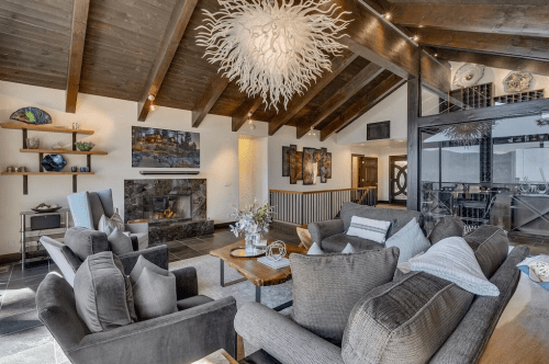 Cozy living room with a fireplace, modern decor, wooden beams, and a unique chandelier.