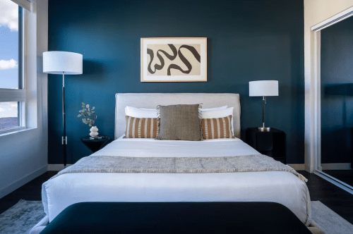 Modern bedroom with a dark blue wall, a queen bed, decorative pillows, and stylish lamps on either side.