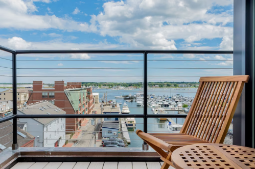 A wooden chair on a balcony overlooking a marina with boats and a cloudy blue sky.