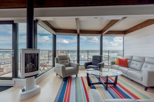 Modern living room with large windows, a cozy fireplace, and a view of the harbor, featuring a striped rug and stylish furniture.
