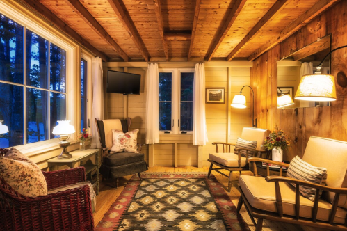 Cozy interior of a cabin with wooden beams, two armchairs, a small table, and warm lighting.