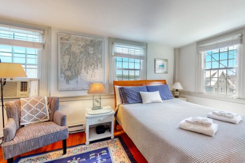 Cozy bedroom with a bed, armchair, lamp, and a large map on the wall, featuring bright windows and natural light.