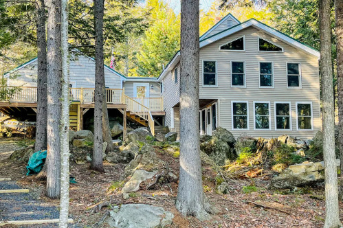 A modern house nestled among trees and rocks, featuring large windows and a deck.