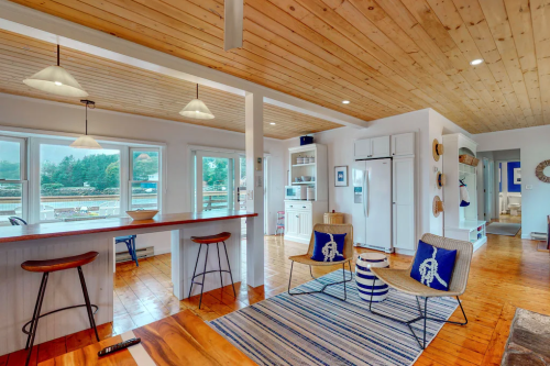 Bright, modern interior with wooden ceiling, bar seating, and nautical decor, featuring large windows and a cozy atmosphere.