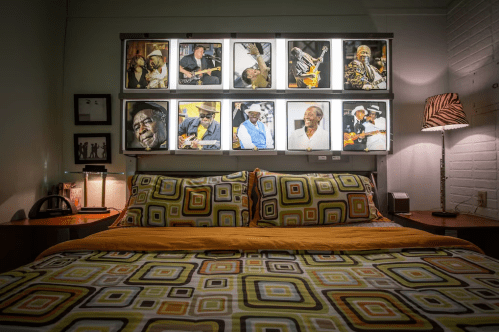 A cozy bedroom with a patterned bedspread and framed photos of musicians on the wall above the bed.