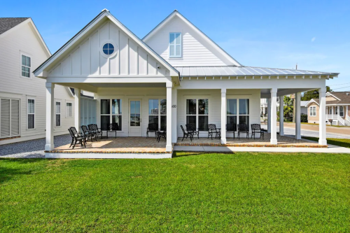 A modern white house with a porch, surrounded by green grass and a clear blue sky.