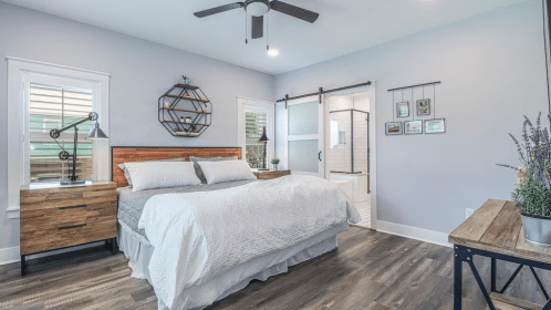Modern bedroom featuring a wooden bed, nightstands, and a sliding barn door, with natural light and stylish decor.