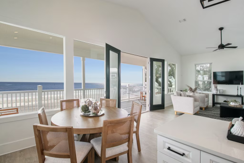 Bright coastal living space with a dining table, large windows, and a view of the ocean. Modern decor and natural light.