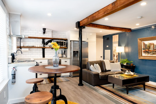 A modern kitchen and living area with wooden beams, a round table, leather sofa, and decorative artwork.