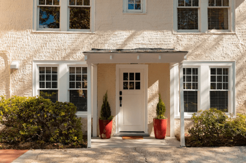 A charming entrance with a white door, surrounded by large windows and potted plants in red containers.