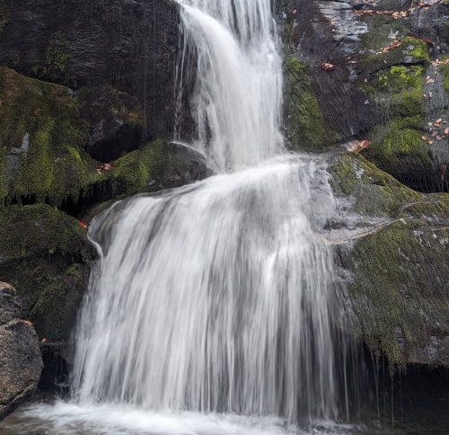 A serene waterfall cascading over moss-covered rocks, surrounded by lush greenery.