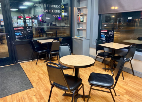 Interior of a cafe with empty tables and chairs, large windows showing a nighttime street view outside.