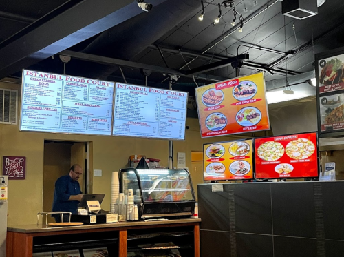Interior of a food court with menus displayed on the wall and a counter, featuring various food options.