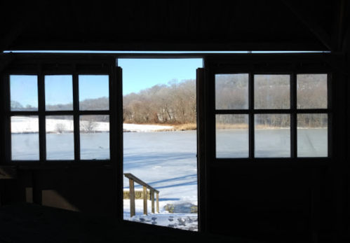 View of a frozen lake and snowy landscape through open double doors.