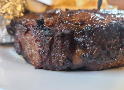 Close-up of a juicy, grilled steak with a charred exterior, served on a white plate.